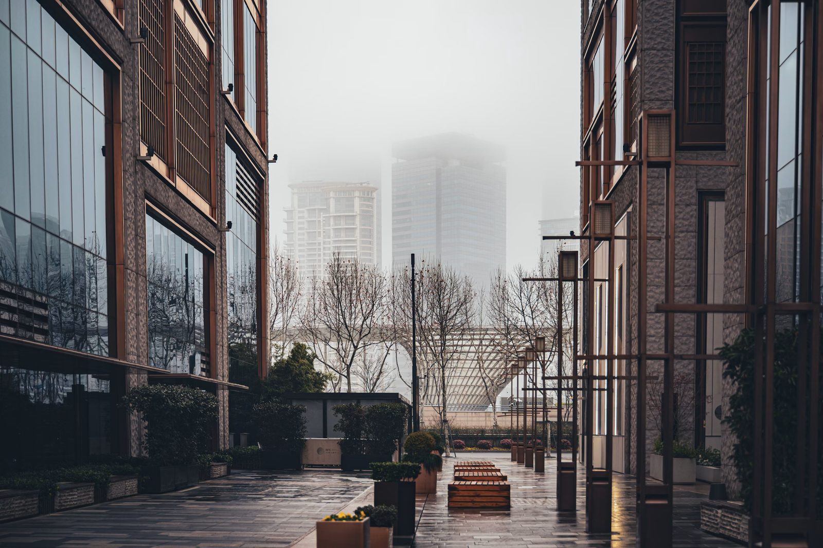 Fog settling over a quiet city plaza between two glass and copper office buildings